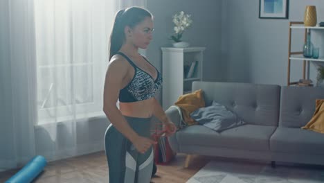 Close-Up-of-a-Fit-Beautiful-Female-in-an-Athletic-Top-Doing-Squat-Exercises-in-Her-Bright-and-Spacious-Living-Room-with-Minimalistic-Interior.