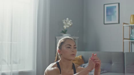 Close-Up-of-a-Fit-Beautiful-Busty-Girl-in-an-Athletic-Top-Doing-Squat-Exercises-in-Her-Bright-and-Spacious-Living-Room-with-Minimalistic-Interior.