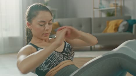 Slow-Motion-Close-Up-Shot-of-a-Beautiful-Confident-Busty-Fitness-Woman-in-an-Athletic-Top-is-Doing-Abdominal-Exercises-in-Her-Bright-and-Spacious-Living-Room-with-Modern-Interior.