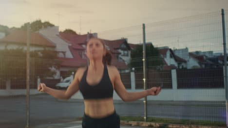 Schöne-energetische-Fitness-Girl-überspringen/springen-Seil.-Sie-ist-ein-Training-in-einem-eingezäunten-Basketballfeld-im-freien-tun.-Am-Nachmittag-Filmmaterial-nach-Regen.