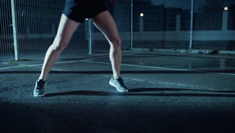 Cerca-de-una-chica-de-hermoso-aptitud-energética-haciendo-pies-corriendo-taladro.-Ella-está-haciendo-un-entrenamiento-en-una-cancha-de-baloncesto-al-aire-libre-cercado.-Imágenes-de-la-noche-después-de-la-lluvia-en-una-zona-residencial-del-barrio.