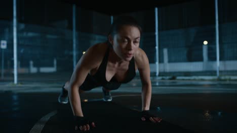 Exhausted-Beautiful-Sporty-Fitness-Girl-Doing-Push-Up-Exercises.-She-is-Doing-a-Workout-in-a-Fenced-Outdoor-Basketball-Court.-Night-Footage-After-Rain-in-a-Residential-Neighborhood-Area.