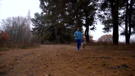 Sportliche-Frau-mit-Hund-im-herbstlichen-Wald-joggen