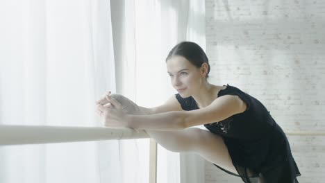 Primer-plano-de-una-joven-y-hermosa-bailarina-haciendo-estiramientos-en-la-barra-de-la-pierna.-En-una-mañana-soleada-en-un-estudio-de-amplia-y-luminosas.-En-cámara-lenta.