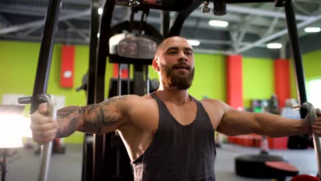 Guapo-hombre-deportivo-está-haciendo-ejercicio-mirando-a-la-cámara-en-el-club-de-fitness