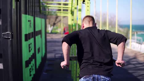 Sports-lifestyle,-street-workout.-Muscular-man-pulls-up-on-the-bar.-Shot-in-4k.-View-from-the-back