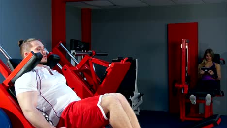 Young-man-and-woman-with-tablet-doing-leg-exercises-in-the-gym