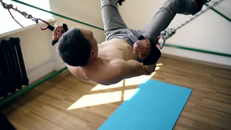 Young-man-doing-exircise-on-quartering-yoga-equipment-and-pull-his-arms-and-legs-with-ropes