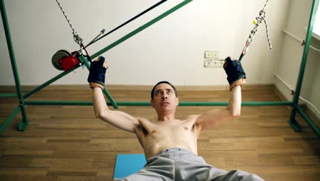 Young-man-doing-exircise-on-quartering-gym-equipment-and-pull-his-arms-and-legs-with-ropes