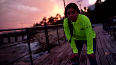 Tired-woman-runner-listening-to-music-on-jetty