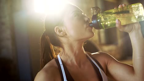 Starke-sportliche-Frau-Getränke-aus-einer-Wasserflasche-nach-anstrengenden-Cross-Fitness-Bodybuilding-Training-in-ihrem-Lieblings-Turnhalle.