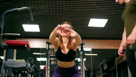 Close-up-of-woman-doing-back-squat-backed-up-by-her-personal-instructor-in-the-gym.-Young-girl-exercising-doing-squats-while-her-trainer-is-watching-her-technique.-Shot-in-4k