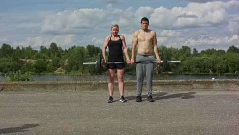 Young-happy-sports-couple-working-out-with-barbell-together