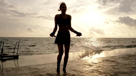 Joven-trabajando-hacia-fuera-en-el-saltar-la-cuerda-contra-el-sol-en-la-playa-en-slowmotion.-Destello-de-lente.-Niña-saltando-sobre-una-cuerda-de-saltar-por-el-mar.-Rodada-en-4k