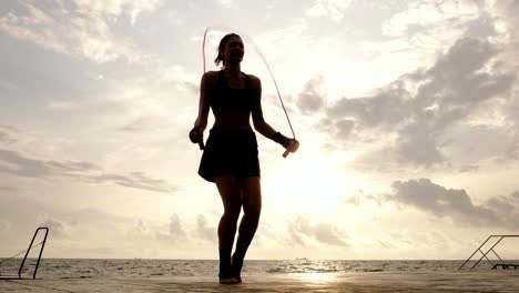 Formular-unten-anzeigen:-junge-Frau,-die-Arbeiten-auf-dem-Springseil-gegen-die-Sonne-am-Strand-in-Slowmotion.-Linseneffekt.-Mädchen-am-Meer-auf-einem-Springseil-Springen.-Schuss-in-4k