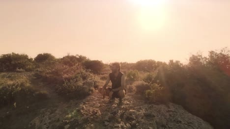 Man-in-workout-clothes-sits-on-top-of-a-cliff-on-an-island-admiring-the-landscape