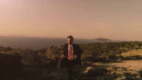 Man-in-elegant-suit-with-briefcase-running-on-top-of-a-cliff-on-an-island-and-exulting