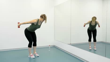 Young-woman-with-dumbells-makes-exercises-for-arms-in-front-of-mirror