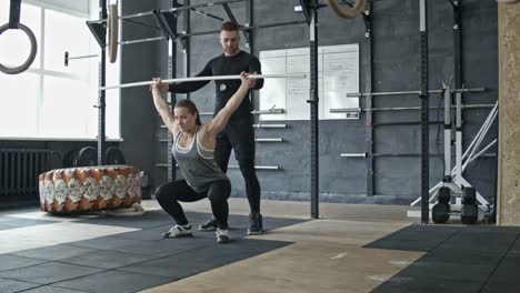 Personal-Trainer-Helping-Woman-Doing-Barbell-Squats