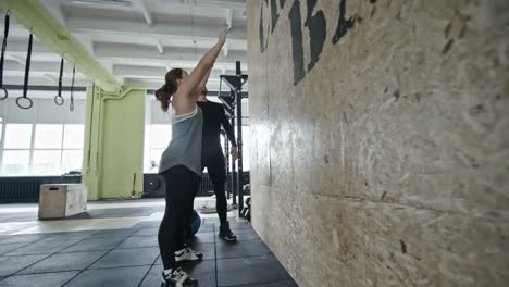 Entrenador-personal-apoyo-a-mujer-durante-el-ejercicio-de-tiro-de-bola-de-pared