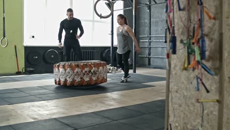 Mujer-realizando-neumático-invierte-en-entrenamiento-Personal-con-el-entrenador