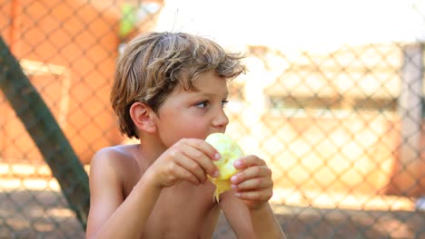 Cándido-retrato-de-niño-guapo,-comer-una-naranja-fuera-en-4K