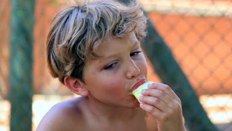 Primer-plano-de-niño-comiendo-fruta-saludable-al-aire-libre-en-la-luz-del-sol.-Joven-comiendo-naranjas-fuera-de-la-luz-del-sol-en-4K