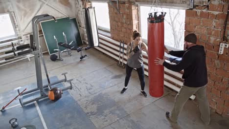 Hembra-Boxer-golpear-saco-durante-el-entrenamiento-con-entrenador