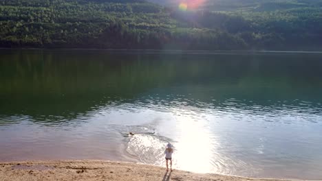 Frau-spielt-mit-ihrem-Hund-in-der-Nähe-Fluss-Küste-an-einem-sonnigen-Tag-4K-4k