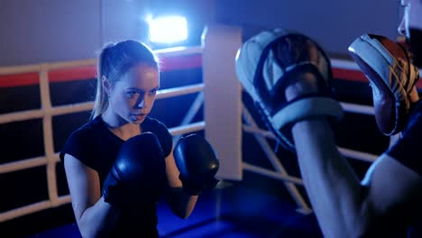 Athletic-woman-trains-her-punches-on-the-bag,-which-is-held-by-her-partner,-coach.-Strong-and-gorgeous-woman-exercising-in-the-gym.