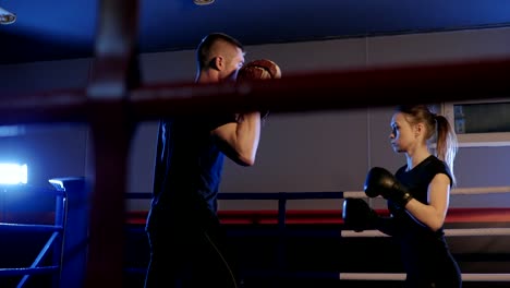 Sportliche-Frau-trainiert-ihre-Schläge-auf-die-Tasche,-die-von-ihrem-Partner,-Trainer-gehalten-wird.-Starke-und-wunderschöne-Frau-Turnen-in-der-Turnhalle.