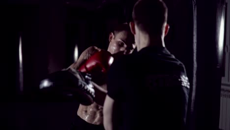 Boxer-man-hits-punching-bag-with-his-fists.-Trainer-Holds.-Boxer-hits-punching-bag-that-her-partner.Part-of-his-gym-training.-Fighter-training-with-punching-bag