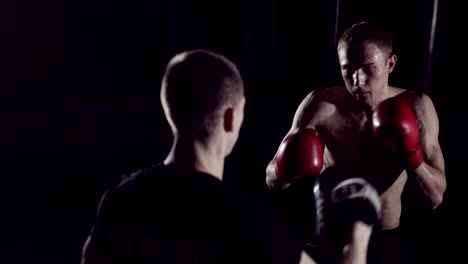 Boxer-man-hits-punching-bag-with-his-fists.-Trainer-Holds.-Boxer-hits-punching-bag-that-her-partner.Part-of-his-gym-training.-Fighter-training-with-punching-bag