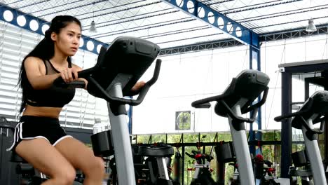 young-woman-execute-exercise-in-fitness-center.-female-athlete-riding-stationary-bicycle-in-gym.-sporty-asian-girl-working-out-in-health-club.