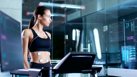 Beautiful-Woman-Athlete-Wearing-Sports-Bra-with-Electrodes-Connected-to-Her,-Walks-on-a-Treadmill-in-a-Sports-Science-Laboratory.-In-the-Background-Laboratory.-Medium-Shot.