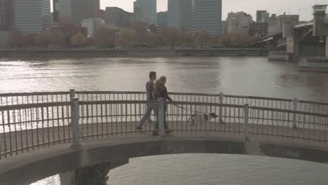 Jóvenes-amantes-de-la-pareja-paseando-su-perro-adorable-en-un-puente-al-atardecer