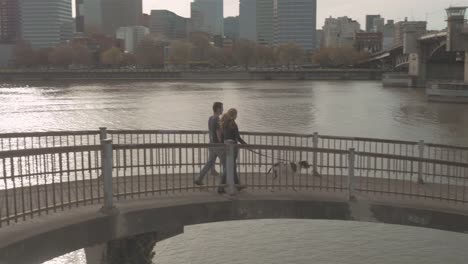 Young-loving-couple-walking-their-adorable-dog-on-a-bridge-at-sunset