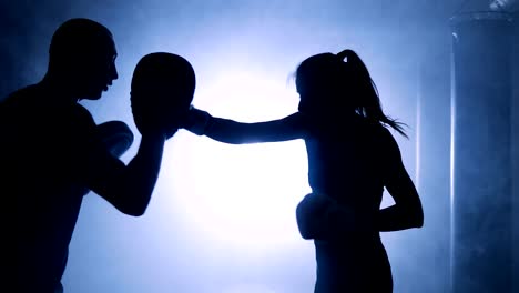 Silhouettes-of-a-female-boxer-punching-a-boxing-bag-with-boxing-gloves-in-a-smoky-gym