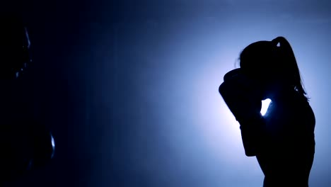 Silhouettes-of-a-woman-boxer-trains-her-punches-on-a-punching-bag-that-her-partner-in-dark-gym