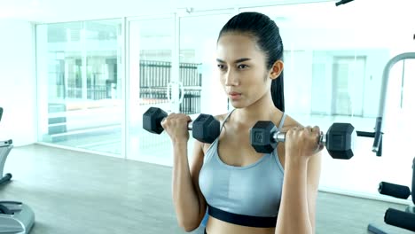 Sporty-young-asian-woman-exercising-with-dumbbells-in-the-gym.-Woman-exercise-at-fitness-gym.-Sport-and-Reaction-concept.-4k-Resolution.