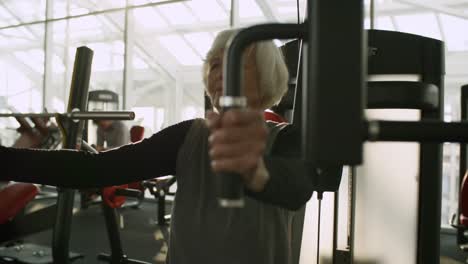 Mujer-Senior-entrenamiento-en-máquina-de-la-prensa-de-pecho-en-el-gimnasio