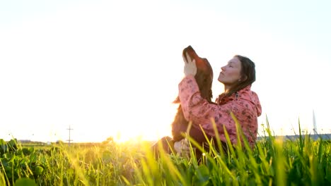 Mujer-jugando-con-el-perro-al-atardecer,-niña-con-mascota-sentados-sobre-la-hierba-y-relajante-en-la-naturaleza