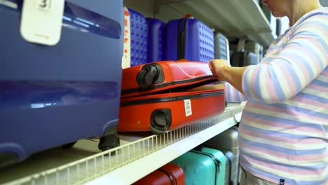 Caucasian-woman-near-shop-shelves-choosing-suitcase-in-haberdashery-market