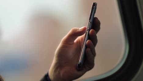 Close-up-of-hands-holding-smartphone-device-with-blurred-background-landscape-in-motion.-Person-surfing-the-internet-and-checking-emails-while-commuting-by-train