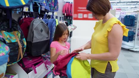 Caucasian-mother-and-daughter-near-shop-shelves-choosing-school-bag-backpack-in-haberdashery-market