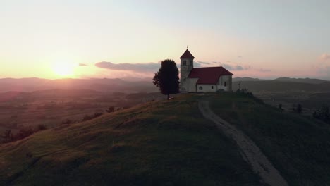 Revealing-shoot-of-a-Catholic-church-on-a-hill-with-a-beautiful-view-to-the-village-in-summertime-in-the-sunset