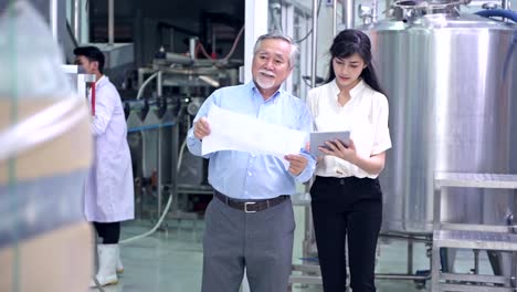 Factory-owner-inspecting-his-production-line.-Asian-senior-man-with-beautiful-asian-female-personal-assistant-talking-inside-factory.