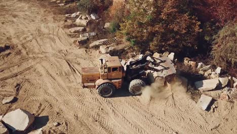 professional-bulldozer-with-a-bucket-is-spreading-sand-near-the-stones-on-the-background-of-the-quarry.