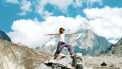 Young-woman-performs-a-basic-warrior-asana-in-yoga-against-the-backdrop-of-a-snowy-mountain-in-a-hike.-Girl-does-gymnastics-and-gymnastics-on-fresh-air-in-a-hike-on-the-nature