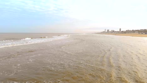 Vista-aérea.-Cámara-lenta-vuelo-sobre-el-mar-y-las-olas-que-llegan-a-la-orilla-en-la-soleada-mañana.-Zandvoort-Holanda.-Mar-del-norte.-Línea-de-Costa